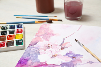 Beautiful floral picture, brushes and watercolor paints on light table, closeup