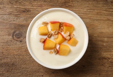 Tasty peach yogurt with granola and pieces of fruit in bowl on wooden table, top view