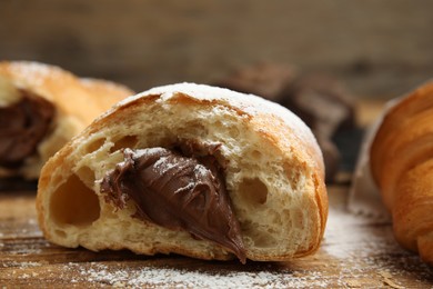 Tasty croissant with chocolate and sugar powder on wooden table, closeup