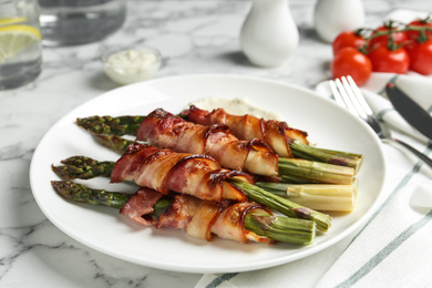 Oven baked asparagus wrapped with bacon on white marble table