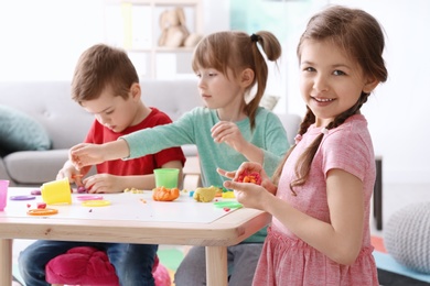 Cute little children using play dough at table indoors