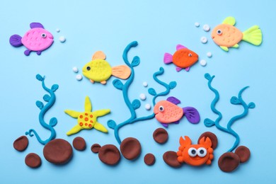 Photo of Colorful fish, water plants and stones made with play dough on light blue background, flat lay