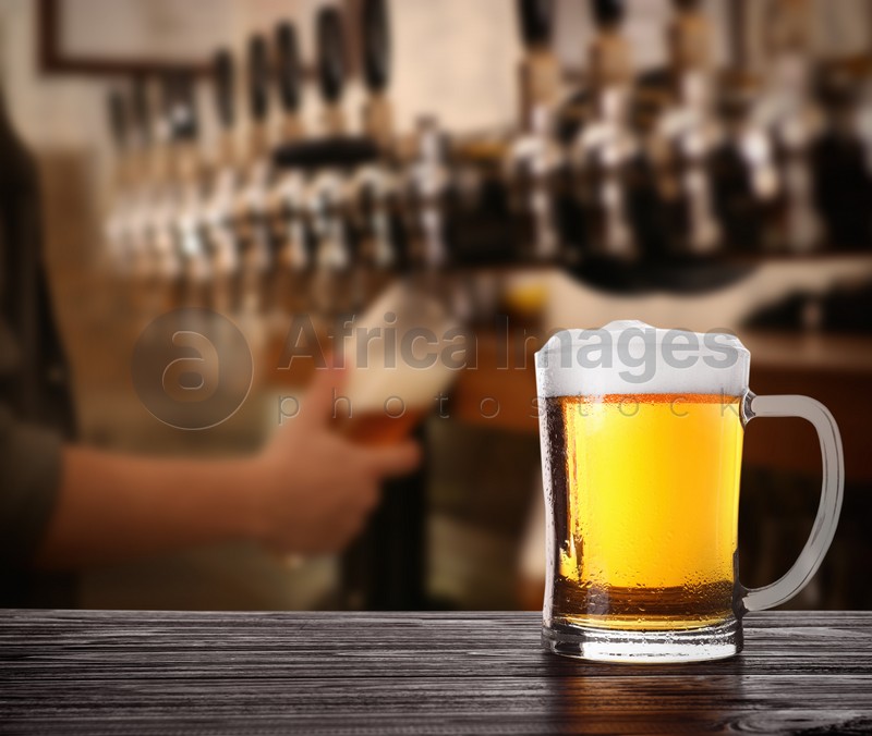 Fresh cold beer on wooden table and bartender in pub, space for text 
