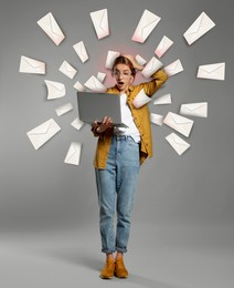 Email spam. Emotional young woman with laptop and many letters on grey background