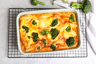 Tasty broccoli casserole in baking dish on cooling rack, flat lay