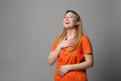 Beautiful young woman laughing on grey background, space for text. Funny joke