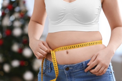 Woman with measuring tape indoors, closeup. Overweight problem after New Year party