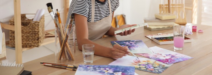 Young woman drawing flowers with watercolors at table indoors, closeup. Banner design