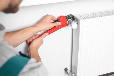 Professional plumber using adjustable wrench for installing new heating radiator indoors, closeup