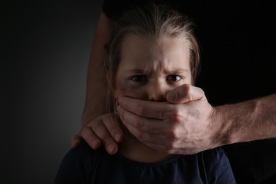 Man covering scared little girl's mouth on black background. Domestic violence