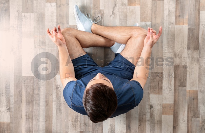 Young man sitting on floor and practicing zen yoga, top view