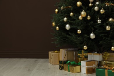 Beautifully decorated Christmas tree and many gift boxes near brown wall indoors, space for text