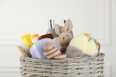 Wicker basket full of different baby cosmetic products, accessories and toys on blurred background, closeup