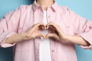 Woman making heart with hands on light blue background, closeup
