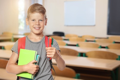 Image of Little boy with school stationery in empty classroom