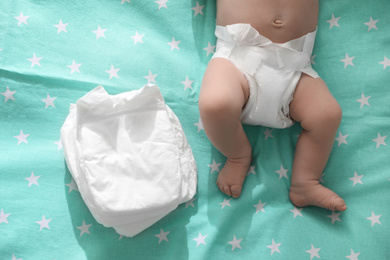 Cute little baby in diaper lying on bed, top view