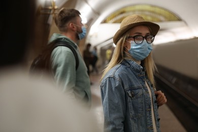 Young woman in protective mask at subway station, space for text. Public transport