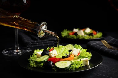 Dressing tasty fresh Greek salad with olive oil on dark table
