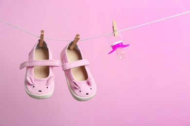 Small shoes and pacifier hanging on washing line against color background, space for text. Baby accessories