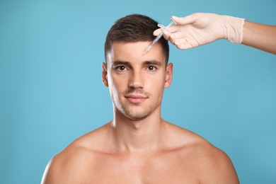 Man getting facial injection on light blue background. Cosmetic surgery