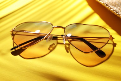 Stylish elegant heart shaped sunglasses on yellow background, closeup