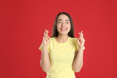 Excited young woman holding fingers crossed on red background. Superstition for good luck