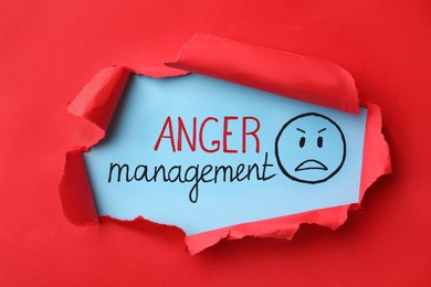 Text Anger Management and drawn angry face on light blue background, view through torn red paper