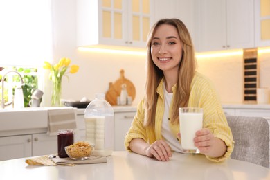 Young woman with gallon bottle of milk, glass and breakfast cereal at white table in kitchen