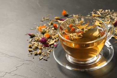 Photo of Freshly brewed tea and dried herbs on black table. Space for text