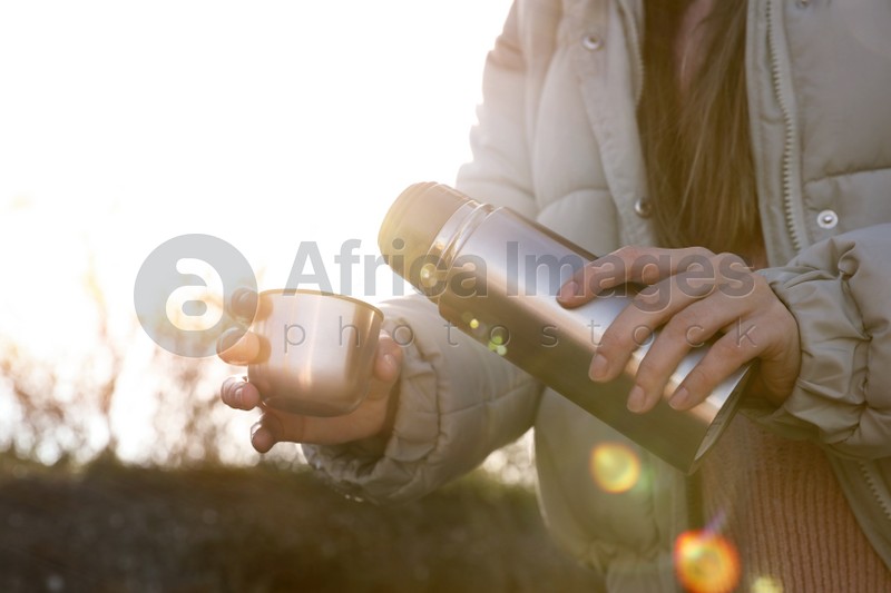 Photo of Woman pouring hot drink into cup from thermos outdoors, closeup