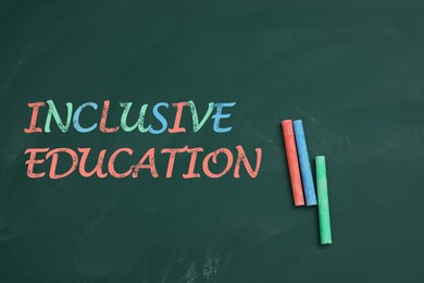 Phrase INCLUSIVE EDUCATION and colorful chalks on green board, flat lay