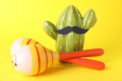 Photo of Colorful maracas, toy cactus with mustache on yellow background. Musical instrument