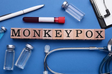 Photo of Flat lay composition with word Monkeypox made of wooden cubes and medical supplies on blue background