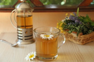 Tasty herbal tea and fresh chamomile flowers on white table