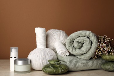 Photo of Composition with different spa products and flowers on beige table against brown background. Space for text