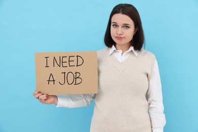 Photo of Young unemployed woman holding sign with phrase I Need A job on light blue background
