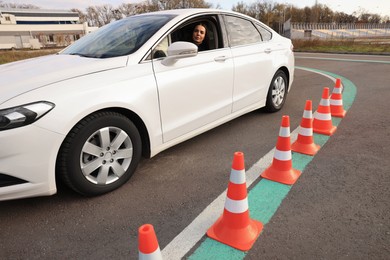 Young woman in car on test track with traffic cones. Driving school
