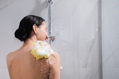 Photo of Young woman with mesh pouf taking shower at home, back view. Space for text