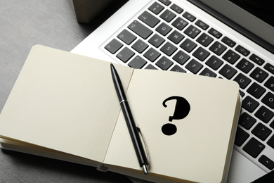 Notebook with question mark, pen and laptop on grey table, closeup