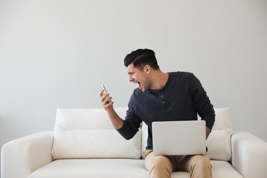 Emotional man with smartphone and laptop at home