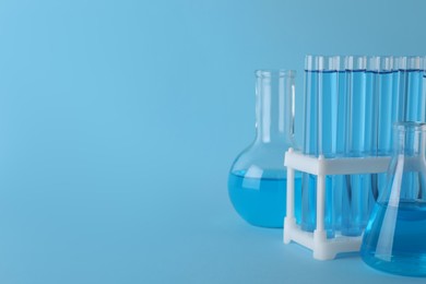 Laboratory glassware with light blue liquid on turquoise background. Space for text