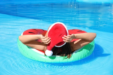 Young woman wearing Santa Claus hat on inflatable ring in swimming pool. Christmas vacation