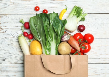Paper bag with fresh vegetables on wooden background, flat lay