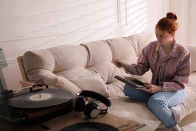 Young woman choosing vinyl disc to play music with turntable at home