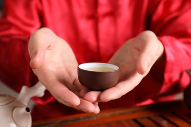 Master offering cup of freshly brewed tea during traditional ceremony at table, closeup