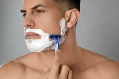 Handsome man shaving with razor on grey background, closeup