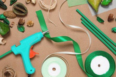 Hot glue gun and handicraft materials on brown background, flat lay