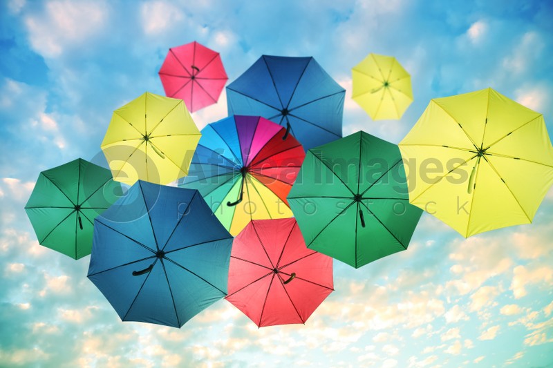 Group of different colorful umbrellas against blue sky with white clouds on sunny day, bottom view