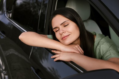 Photo of Happy young woman with closed eyes enjoying trip while lying out of car window