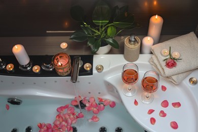Bathtub with glasses of wine and candles indoors, above view. Romantic atmosphere